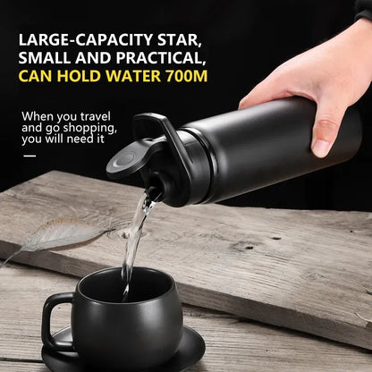 Black insulated water bottle pouring water into matching black cup on wooden table, Aznolt fitness accessory.